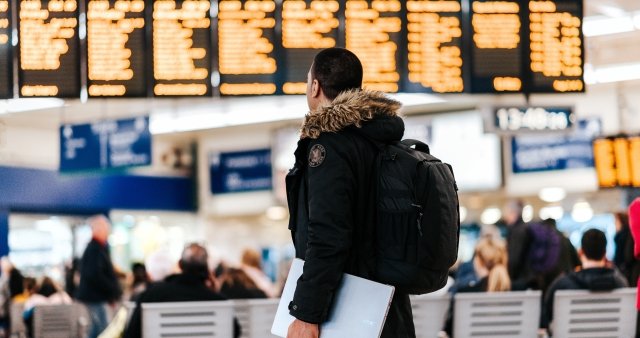 person stands in front of a lit-up arrivals and departures board